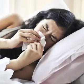A woman lying in bed, blowing her nose due to seasonal allergies